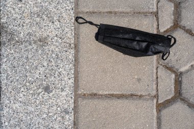 Güneşli bir günde gri kuru asfalt. Siyah bir maskenin düştüğü gün.