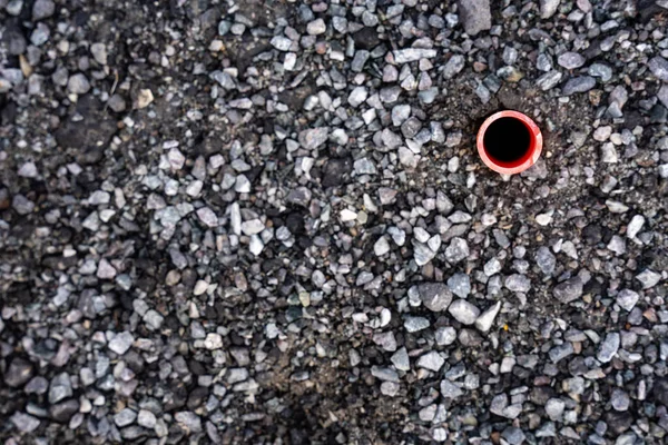 a close-up of a rubble road shows the end of a red tube pierced into the ground
