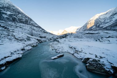 Nehir kışın biraz donar ve kayalık kıyılar kar beyazı olur. Üzerlerinde mavi gökyüzü vardır..