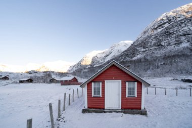 Kışın Norveç 'in karlı dağlarında çitleri olan tahtalardan yapılmış kırmızı ahşap bir ev.