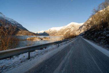 Gri soğuk asfalt sabahın erken saatlerinde Norveç fiyordunun yanında sonbaharda dağlarda zaten beyaz kar var.