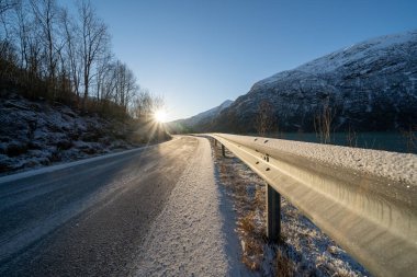 Gri soğuk asfalt sabahın erken saatlerinde Norveç fiyordunun yanında sonbaharda dağlarda zaten beyaz kar var.
