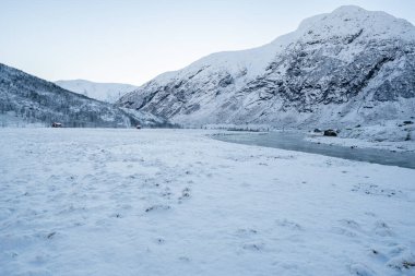 Nehir kışın biraz donar ve kayalık kıyılar kar beyazı olur. Üzerlerinde mavi gökyüzü vardır..