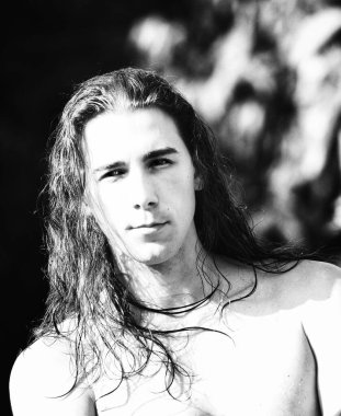 Çok uzun saçlı çekici bir adam vahşi doğada poz veriyor. Modelleme ve Moda Konsepti.