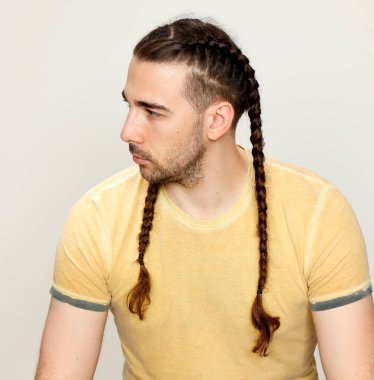 İzole edilmiş arka planda saç örgüleri olan şık bir erkek model. Tarz, saç stili, moda konsepti.