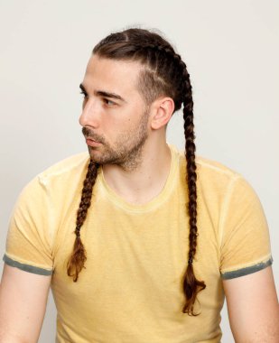 İzole edilmiş arka planda saç örgüleri olan şık bir erkek model. Tarz, saç stili, moda konsepti.