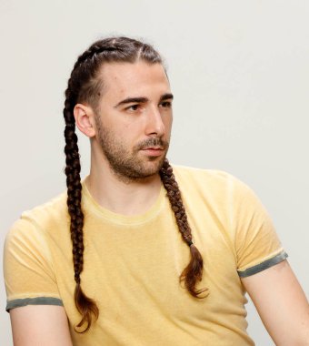 İzole edilmiş arka planda saç örgüleri olan şık bir erkek model. Tarz, saç stili, moda konsepti.