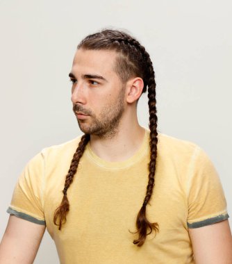 İzole edilmiş arka planda saç örgüleri olan şık bir erkek model. Tarz, saç stili, moda konsepti.