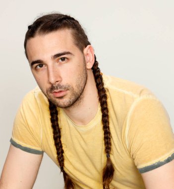 İzole edilmiş arka planda saç örgüleri olan şık bir erkek model. Tarz, saç stili, moda konsepti.