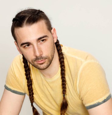 İzole edilmiş arka planda saç örgüleri olan şık bir erkek model. Tarz, saç stili, moda konsepti.