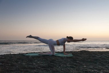 Yoga kavramıyla sağlıklı. Çekici genç kadın gün batımında plajda yoga yapıyor. Rahat ve rahat..