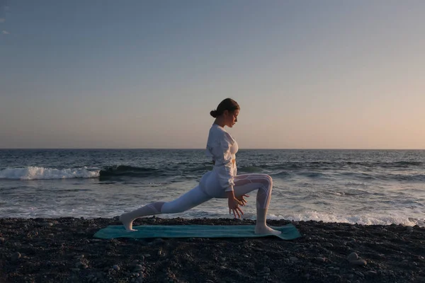 Yoga kavramıyla sağlıklı. Çekici genç kadın gün batımında Yoga 'da Savaşçı Pozu (Virabhadrasana) pratiği yapıyor..