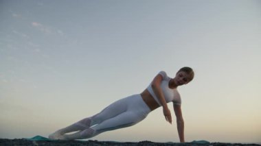 Yoga kavramıyla sağlıklı. Çekici genç kadın gün batımında sahilde Yan Plank Pozu pratiği yapıyor. Vasisthasana. Rahat ve rahat..