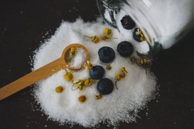 Beyaz şekerli cam kavanoz yaban mersinli ve sarı çiçekli siyah arka plan