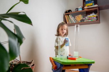 Çocuk evde kimya deneyi yaparken renkli bir sıvıyı test tüpüne döküyor. Evde eğitim ve uzak eğitim