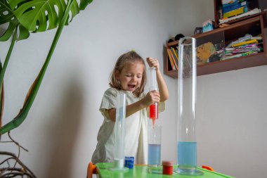 Çocuk evde kimya deneyi yaparken renkli bir sıvıyı test tüpüne döküyor. Evde eğitim ve uzak eğitim