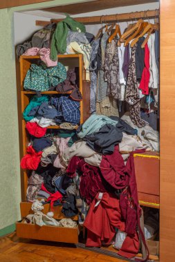 Giysilerle dolu kocaman bir dolap, baştan savma itilmiş ve raflara ve askılara asılmış. Gardırop dağınıklığı. Gardırop dağınıklığı.