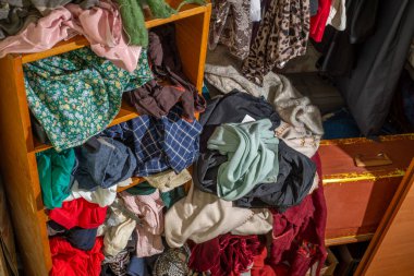 Giysilerle dolu kocaman bir dolap, baştan savma itilmiş ve raflara ve askılara asılmış. Gardırop dağınıklığı. Gardırop dağınıklığı.