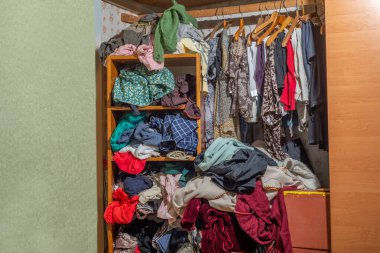 Giysilerle dolu kocaman bir dolap, baştan savma itilmiş ve raflara ve askılara asılmış. Gardırop dağınıklığı. Gardırop dağınıklığı.