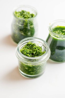 Beyaz arka planda üç kavanozda pesto sosu.