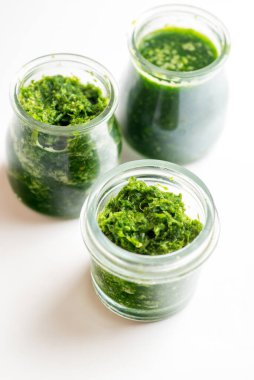 Beyaz arka planda üç kavanozda pesto sosu.