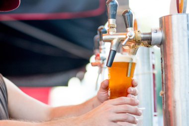 Bira musluktan bardağa dökülür. Barmen birayı plastik bardağa doldurur.