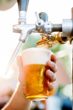 Bira musluktan bardağa dökülür. Barmen birayı plastik bardağa doldurur.
