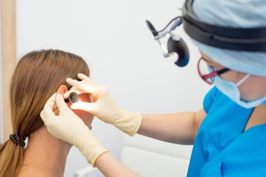 Aletleri, maskesi ve eldivenleri olan bir KBB doktoru hastanın kulaklarını muayene eder. Otolaryngologist onunla