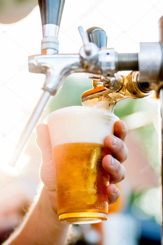 beer is poured into a glass from a tap. The bartender pours beer into a plastic glass