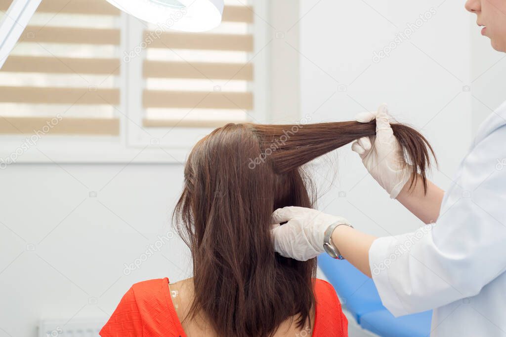 Doctor dermatologist doing hair loss test on female patient with long dark hair. Diagnostics of the hair and scalp diseases