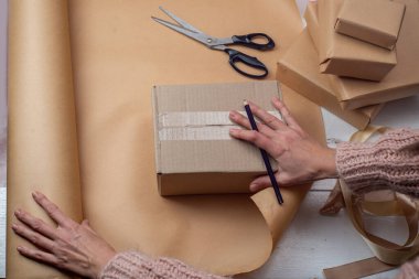 Kraft kağıdına sarılmış hediye paketi. Kraft kağıdına sarılmış hediye paketi. Dişiler kutuları hediyelerle sarar ve parlak kurdelelerden yapılmış papyonlar takar