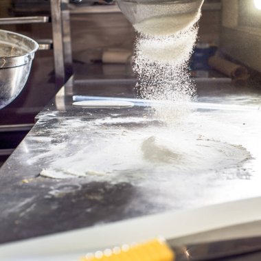 Beyaz un, bir elek aracılığıyla metal bir masaya dökülür. Hamur için un kesiyorum.