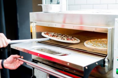 Aşçı pizzacıdaki fırından bitmiş pizzayı alır.