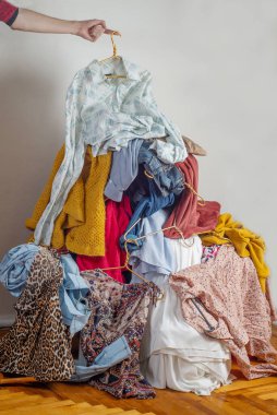 Elbiseleri ikinci el kıyafetlerle dolu bir yığının içine atıyor. Sürdürülebilir moda kavramı. Hafif arka planda kullanılmış giysiler yığını. Geri dönüşüm için ikinci el