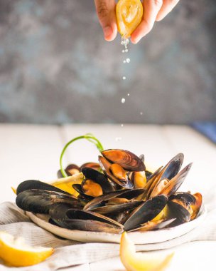 El, kabuğunda midye olan bir tabağın üzerine limon sıkıyor.