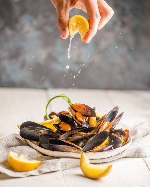 El, kabuğunda midye olan bir tabağın üzerine limon sıkıyor.