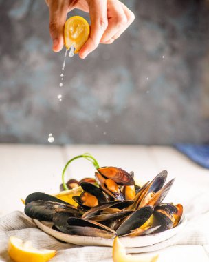 El, kabuğunda midye olan bir tabağın üzerine limon sıkıyor.