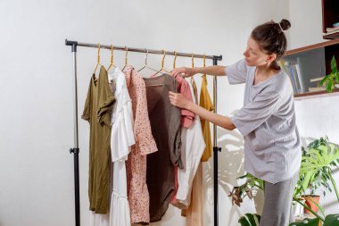 Woman hangs clothes on a rail at home. Sorting wardrobe and second hand. The concept of sustainable living