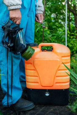 Elektrikli bahçe spreyi ve koruyucu kıyafetli maskeli bir çiftçi. Tarım spreyi. Bahçe Bitkisi Bakım Aracı