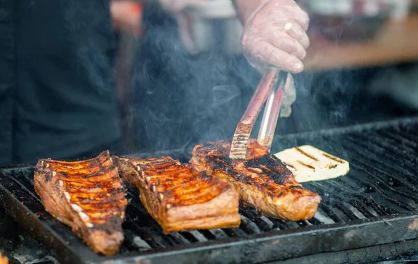 Barbecue ribs. Man in gloves flips grilled ribs on a charcoal grill. Picnic in the backyard during a family holiday. BBQ meat.