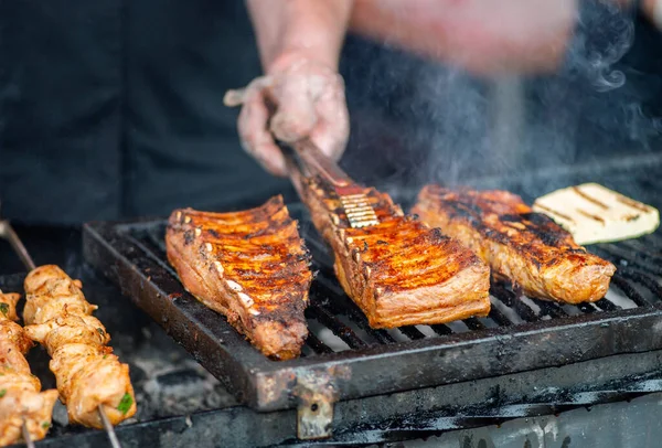 Barbecue ribs. Man in gloves flips grilled ribs on a charcoal grill. Picnic in the backyard during a family holiday. BBQ meat.