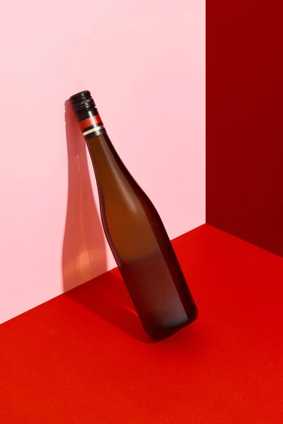 Uma garrafa de vinho encostada à parede. Bebida alcoólica em fundo criativo vermelho e rosa com sombras profundas — Fotografia de Stock