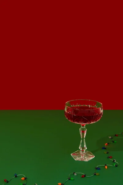 Vánoční novoroční kreativní kompozice se sklenicí červeného šampaňského a gerlandem na červeném a zeleném pozadí — Stock fotografie