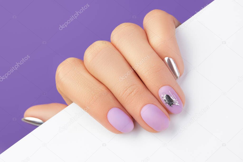 Close up womans hand with matte lavender nail design on purple background
