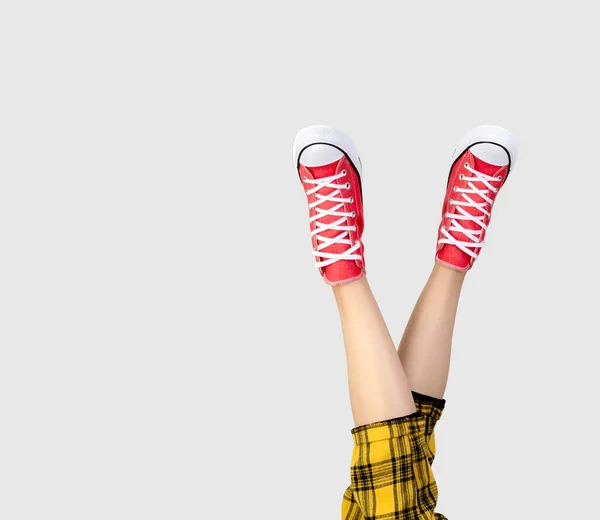 Piernas de una mujer joven en elegantes zapatillas rojas sobre fondo gris. — Foto de Stock