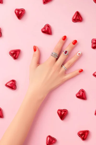 Χειροποίητο γυναικείο χέρι με δαχτυλίδια σε ροζ φόντο. Μοντέρνο κόκκινο καρφί σχεδιασμό με καρδιά — Φωτογραφία Αρχείου