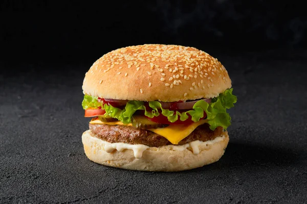 Свіжий смачний бургер на темному тлі. Чізбургер з яловичиною, помідорами, соліннями, салатом і цибулею — стокове фото