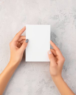 Manikürlü kadın elleri gri beton arka planda kartpostal tutuyor.