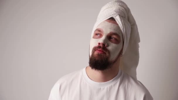 Hombre en camiseta blanca aplicar soporte de máscara facial sobre fondo blanco. Autocuidado procedimiento de spa matutino — Vídeo de stock