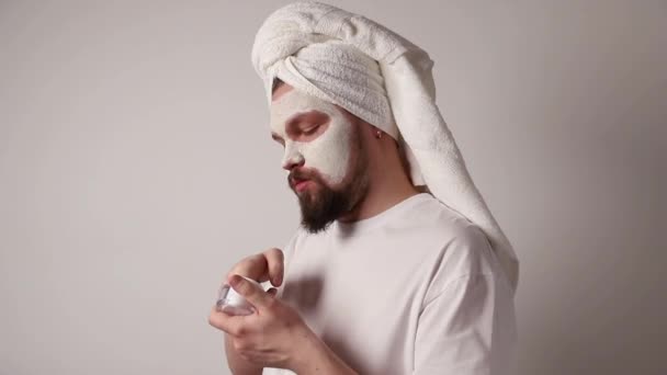 Hombre en camiseta blanca aplicar soporte de máscara facial sobre fondo blanco. Tratamiento de belleza, aseo y concepto de bienestar — Vídeo de stock